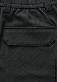Tessuto nero intrecciato con una texture diagonale, dotato di una tasca posteriore rettangolare con bordi cuciti e una vita elastica.