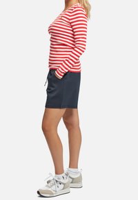 Rot-weiß gestreifte Langarmbluse, kombiniert mit navyblauen Shorts und weißen Turnschuhen mit beigen Akzenten und Schnürsenkeln.
