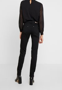 Černé přiléhavé džíny v kombinaci s průhlednou černou blůzkou s červenými puntíky a dlouhými rukávy. Celý vzhled tvoří černé boty na podpatku.