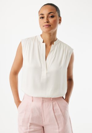 Hvid ærmeløs bluse med V-udskæring og let rynkning ved skuldrene, kombineret med skræddersyede lyserøde bukser med høj talje.