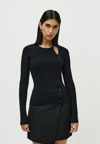 Cardigan negru cu maneci lungi, cu dantelă în jurul g�âtului și detalii cu decupaje, având închidere cu nasturi pe față. Textură fină.