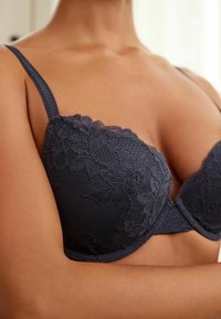 Dunkelblaues Spitzen-BH mit floralen Mustern, gepolsterten Cups und verstellbaren dünnen Trägern mit strukturiertem Oberflächendesign.