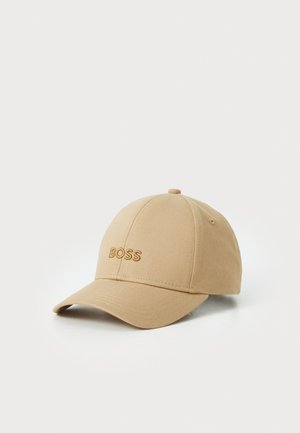 Tan baseball cap with embroidered "BOSS" logo. Features a curved brim, six-panel design, and eyelet ventilation details. Smooth fabric texture.