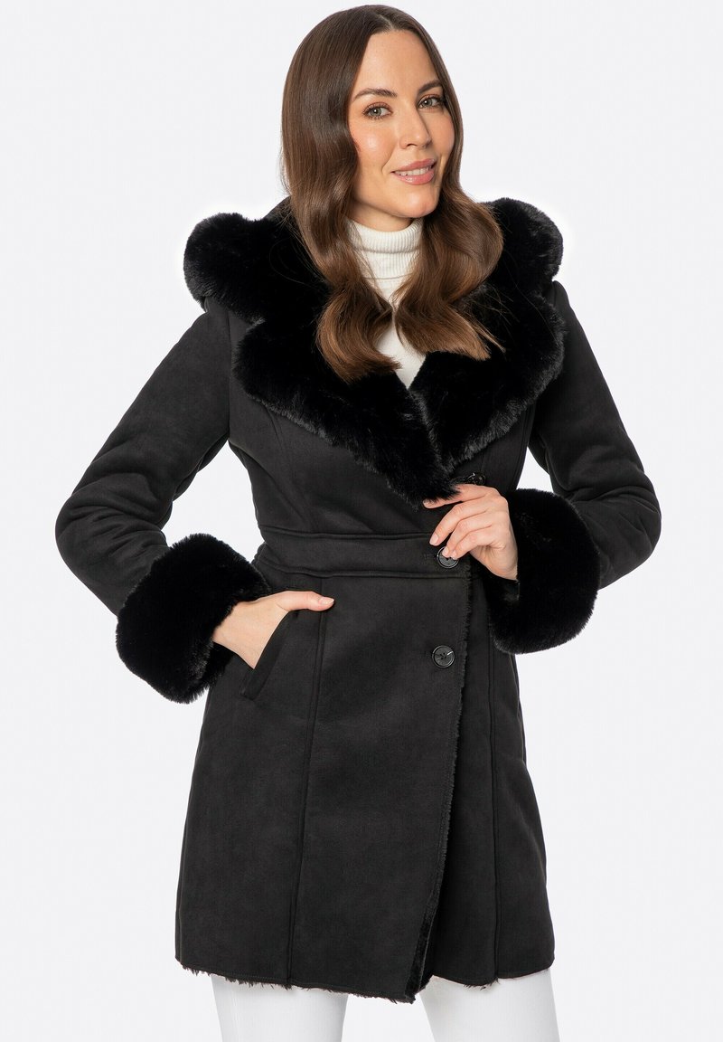 Czarny zamszowy płaszcz z puszystym czarnym kołnierzem i mankietami z futra. Posiada zapięcie na guziki i boczne kieszenie. Gładka faktura i dopasowany krój.