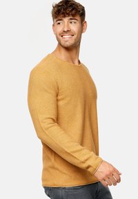 Mustard yellow long-sleeve knitted sweater with a rounded neckline, ribbed cuffs, and side slits; textured fabric with a slightly loose fit.
