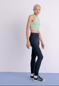 Melni legingi ar augstu jostasvietu, apvienoti ar gaiši zaļu crop topu. Modelis valkā melnas sporta kurpes ar zaļiem akcentiem. Pamatne ir vienkārša.