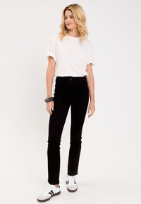 Jeans de mezclilla negra con un diseño ajustado, combinados con una camiseta blanca de mangas arremangadas. Usados con zapatillas blancas y grises.