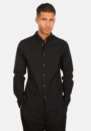 Schwarze Hemdjacke aus glattem Stoff, mit schlanker Passform, spitzem Kragen und subtilen Logo auf der Brust. Lange Ärmel mit Knopfmanschetten.