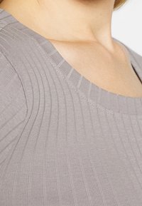 Top grigio a coste con un ampio scollo, caratterizzato da un tessuto testurizzato e dettagli di cucitura delicati. La prima linea mostra la morbidezza del materiale.