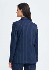 Granatowa marynarka w prążki z dopasowanym krojem, klapami z wcięciem i mankietami na trzy guziki. Gładka struktura tkaniny i zdefiniowany fason.