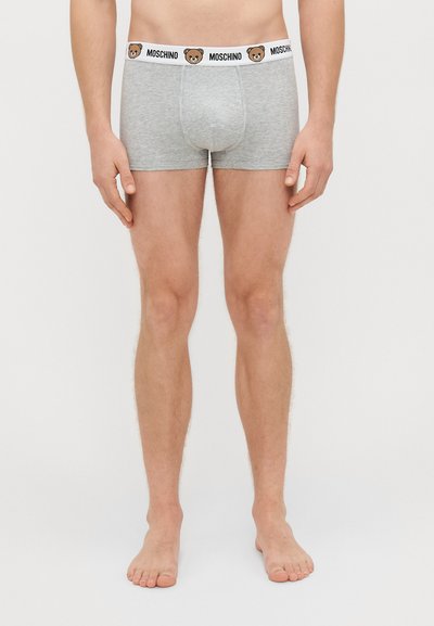 Boxer briefs de algodão cinza com uma cor sólida, apresentando uma cintura preta adornada com um logotipo de urso e o texto "MOSCHINO". Design ajustado.