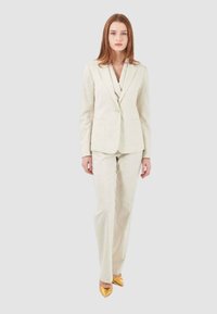 Completo beige su misura con giacca a un bottone e rever a punta, abbinato a pantaloni dritti e tacchi a punta gialli lucidi.
