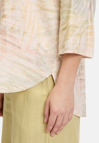 Blusa leggera a fantasia pastello con maniche corte e orlo arrotondato, abbinata a pantaloni di lino verde pallido texture.