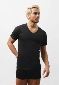 Czarny t-shirt z krótkim rękawem i dekoltem w serek, wykonany z gładkiego materiału, dopasowany krój, noszony z czarnymi szortami, zaprezentowany na jednolitym tle.