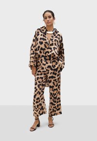 Tenue en imprimé léopard comprenant un haut ample et un pantalon à jambes larges, fabriqués en tissu doux, associés à des sandales noires épaisses et des bijoux audacieux.