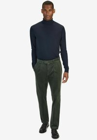 Mörkblå turtleneck-tröja kombinerad med gröna kordbyxor med knapp- och veckdetaljer, avslutat med svarta läderskor.