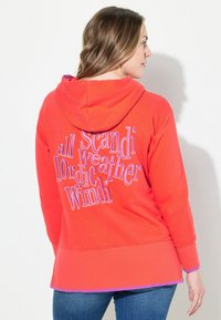 Sudadera con capucha roja y detalles en púrpura. Presenta un ajuste oversized y un texto en la parte posterior que dice "todo el clima nórdico escandinavo es viento".