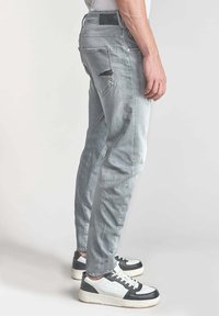 Jasnoszare dżinsy o slim fit, z przetarciami na tylnej kieszeni i gładką teksturą, zestawione z czarno-białymi trampkami.