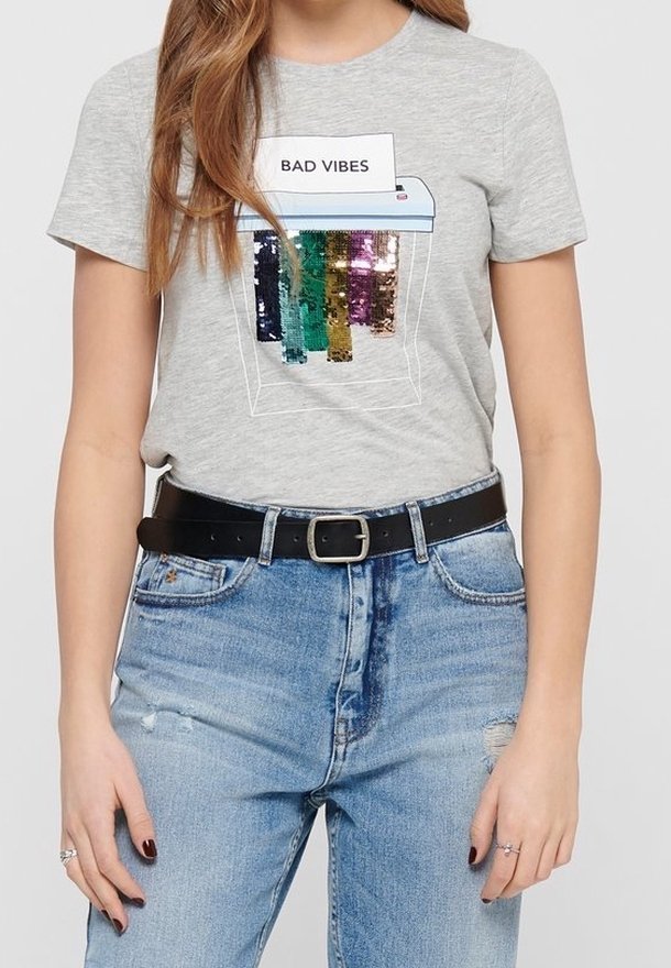 Šedé bavlněné tričko s grafikou "BAD VIBES". Design obsahuje barevné flitrové pruhy. Nosené s modrými roztrhanými džíny a černým opaskem.