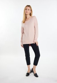 Maglione rosa chiaro a maniche lunghe con orlo a costine e scollatura ampia, abbinato a pantaloni neri aderenti e mocassini neri. Texture liscia.