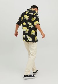 Camicia nera a maniche corte con stampa di limoni gialli e fiori, indossata con pantaloni chiari e scarpe da ginnastica nere.