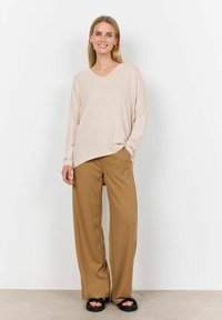 Beige long-sleeve V-neck sweater with a relaxed fit, paired with wide-leg brown trousers and black platform sandals. Smooth textures throughout.
