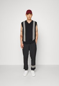 Czarny bezrękawnik w poziome białe paski, połączony z czarnymi spodniami z paskami na mankietach i białymi trampkami.