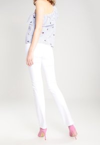 Blau-weißer gestreifter Off-Shoulder-Top mit floralem Stickereimuster, kombiniert mit weißen, figurbetonten Hosen und rosa High-Heels.