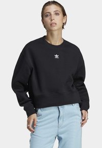 Black cropped sweatshirt made of soft fabric, featuring a round neck and ribbed cuffs. Front displays a small white Adidas logo.
