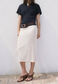 Czarna koszulka polo, kremowa spódnica midi, brązowy skórzany pasek z srebrną klamrą oraz brązowe sandały na koturnie z odkrytymi palcami. Gładkie tekstury, codzienny styl.