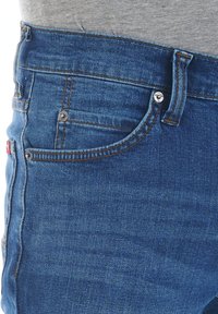 Jeans de denim azul con un corte clásico, con detalles de costura, un bolsillo frontal y un botón de metal. La tela tiene una textura suave.