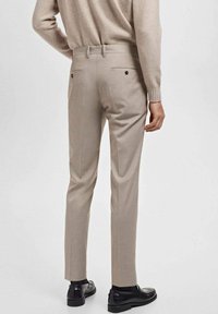 Svetlo bež pasmade hlače z dvema zadnjima �žepoma in temnimi gumbi, z obliko slim fit in ravnim sprednjim delom, v kombinaciji s črnimi čevlji.