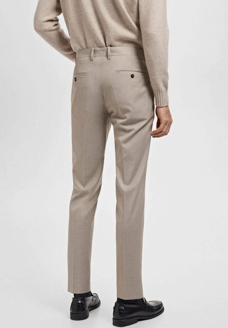 Lyse beige skræddersyede bukser med to baglommer og mørke knapper, der har en slim fit-design og flad front, parret med sorte sko.