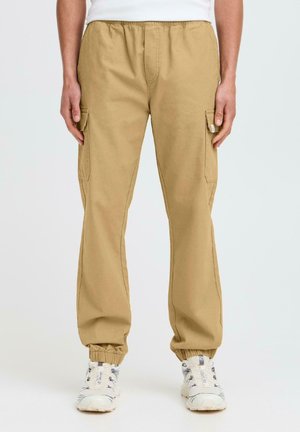 Beige Cargo-Hosen mit elastischem Bund und Bündchen, ausgestattet mit Seitentaschen. Der Stoff ist glatt, strapazierfähig und für Komfort ausgelegt.
