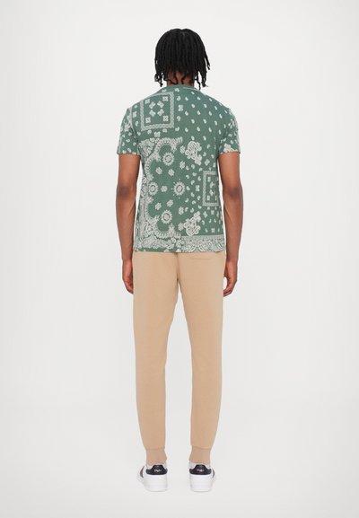 Groen gemêleerd T-shirt met korte mouwen, voorzien van bloemen- en paisleypatronen, gecombineerd met beige taps toelopende broek en witte sneakers.