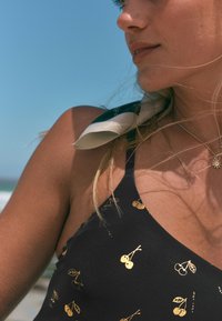 Črno kopalke z zlatim potiskom češenj, z tankimi naramnicami in okroglim izrezom. Gladek, raztegljiv material z mehko teksturo.