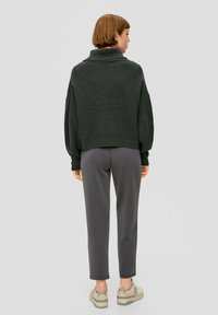 Dunkelgrüner gestrickter Pullover mit umschlagbarem Kragen, kombiniert mit grauen Slim-Fit-Hosen und hellen Sneakers. Sichtbare Falten an den Schultern.