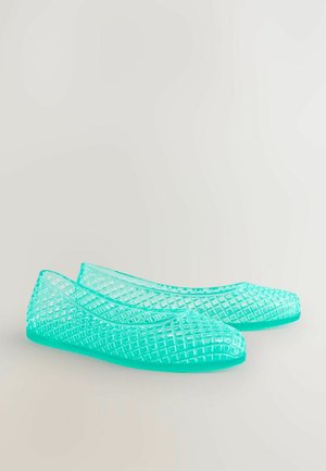 Caurredz, tirkīza krāsas plakanas kurpes ar ģeometrisku, atvērtu audumu un noapaļotiem pirkstiem. Izgatavotas no elastīga plastmasas materiāla.