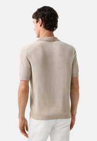 Beige kortærmet polo skjorte lavet af struktureret strikstof. Har en klassisk krave og ribbede manchetter, med en lige søm forneden.
