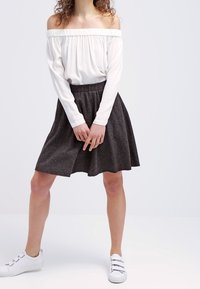 Top blanco de manga larga y con los hombros al descubierto, combinado con una falda acampanada de color gris oscuro, y terminado con zapatillas blancas. Tejido suave y diseño relajado.