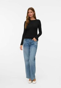 Svart långärmad topp som är ihopparad med ljusblå löst sittande jeans. Fötterna pryds av ljusa ballerinaskor. Enkel design, mjuk tygtextur.