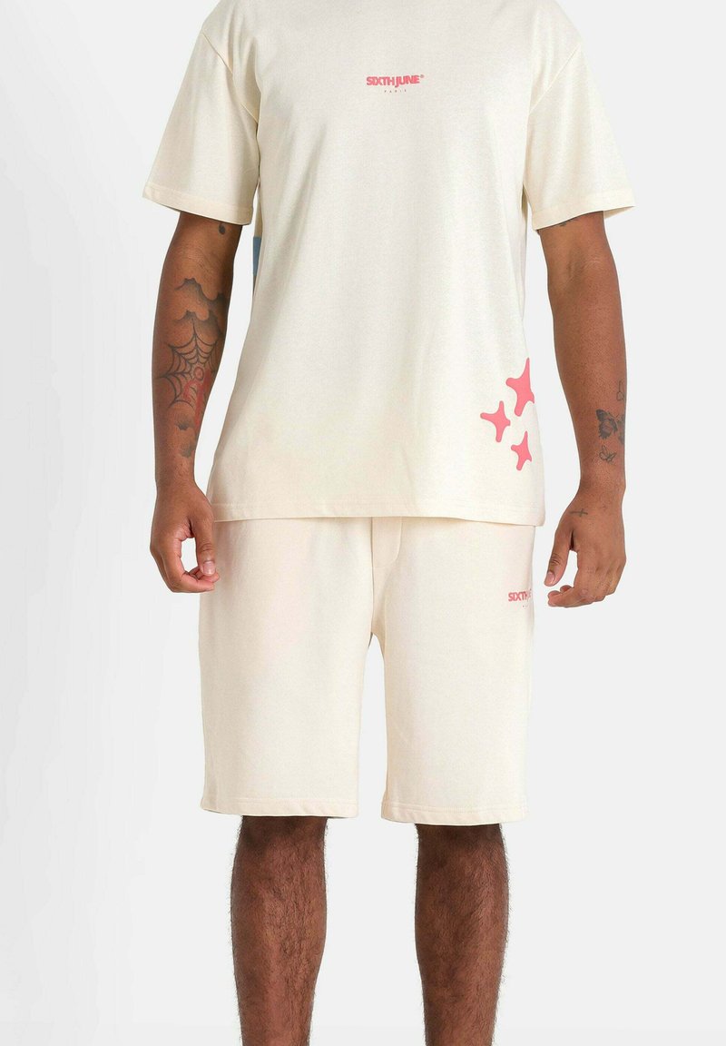 Beige cotton t-shirt and shorts set featuring a small pink logo on the chest and pink abstract patterns on the shorts.