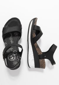 Sandales compensées noires avec brides réglables à la cheville, semelles intérieures imprimé floral et semelles compensées blanches et liège tachetées.