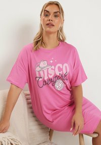 Rosa bomulls t-shirt klänning med ett grafiskt motiv som säger "DISCO Cowgirl," en cowboyhatt och en illustration av en discokula. Löst sittande och korta ärmar.