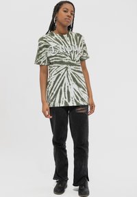Green tie-dye t-shirt with spiral pattern and white "Tupac" text, paired with black ripped jeans and black lace-up shoes.