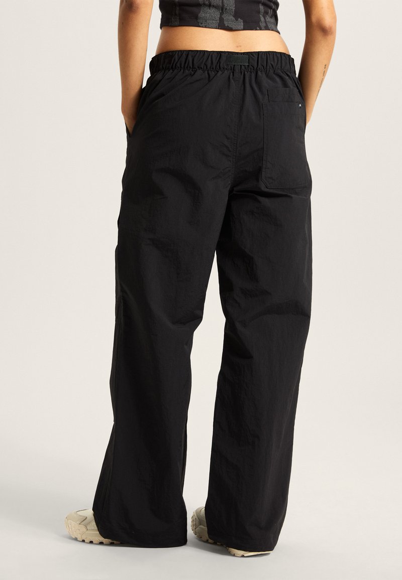 Pantalones negros de pierna ancha con una cinturilla elástica fruncida, hechos de una tela liviana, que cuentan con bolsillos laterales y un acabado texturizado.