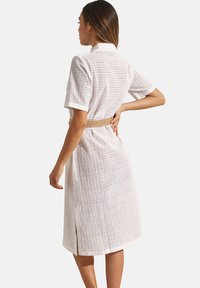Witte jurk met korte mouwen, een gestructureerd patroon, een ceintuur op de taille en zijsplitten. Heeft een klassieke kraag en is knie-lengte.