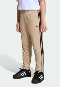 Beige athletic pants with black side stripes and an Adidas logo. Made from soft fabric, featuring an elastic waistband and fitted design.