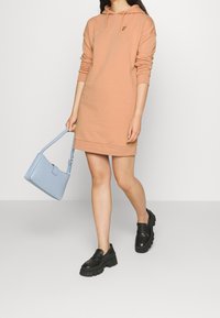 Vestido sudadera con capucha en color melocotón, de mangas largas y con bolsillo frontal; combinado con un bolso estructurado en azul claro y zapatos de plataforma negros.