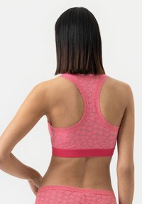 Růžový krajkový bralet s racerback designem, vlnkovými okraji a kontrastním páskem na spodní straně; jemná textura a květinový vzor.